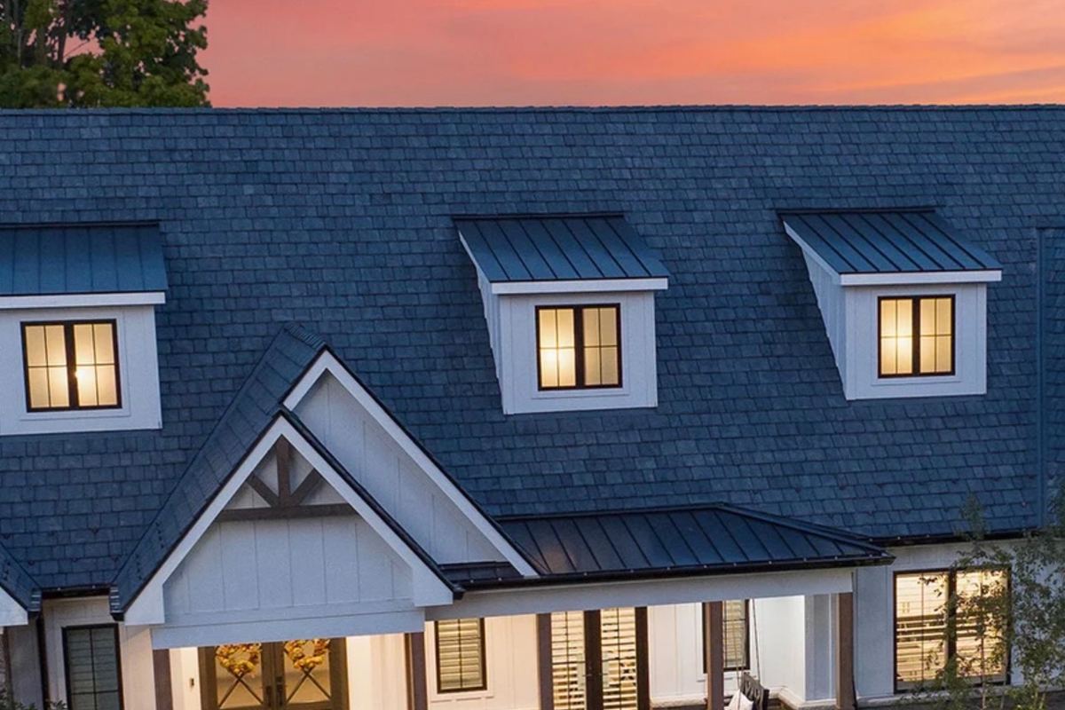 Custom home with composite shake roofing and standing-seam metal dormer accents at dusk